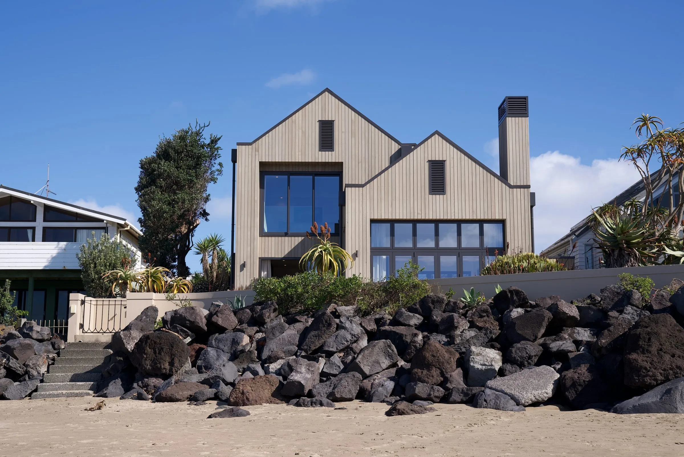 Milford Beach home seen from the beach, with timber-clad gables above the rock wall