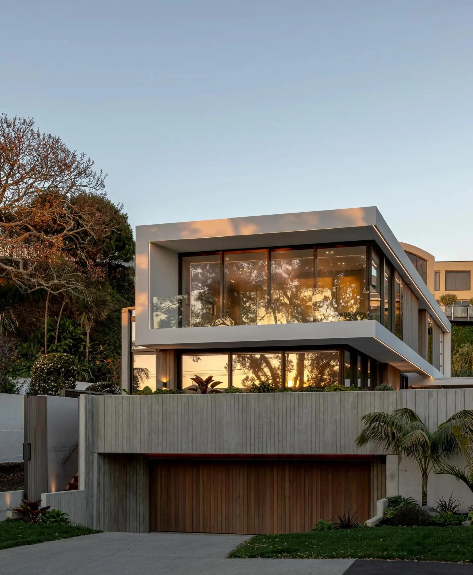 Two-storey home glowing at dusk above a board-formed wall